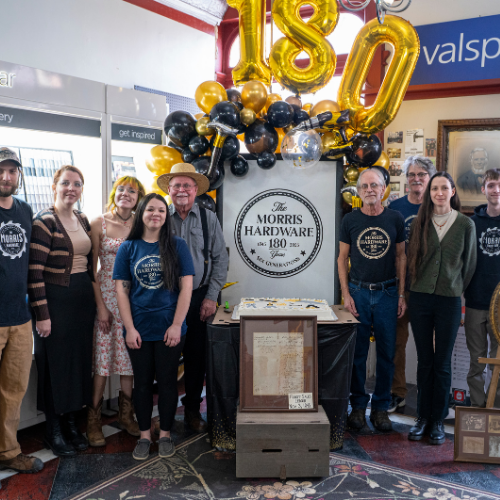 A group of people stand in a hardware store, smiling beside a large 